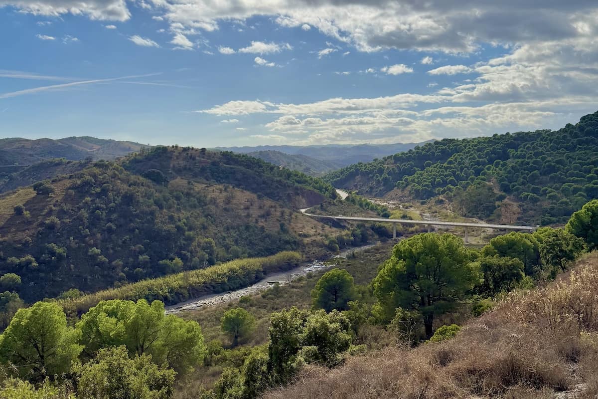 Vista panoramica sobre a Ribeira da Foupana no sotavento algarvio. Estrada e ponte que atravessa o vale, paisagem de serra, colinas verdes e ceu azul. Rota de mota interior Algarve.
